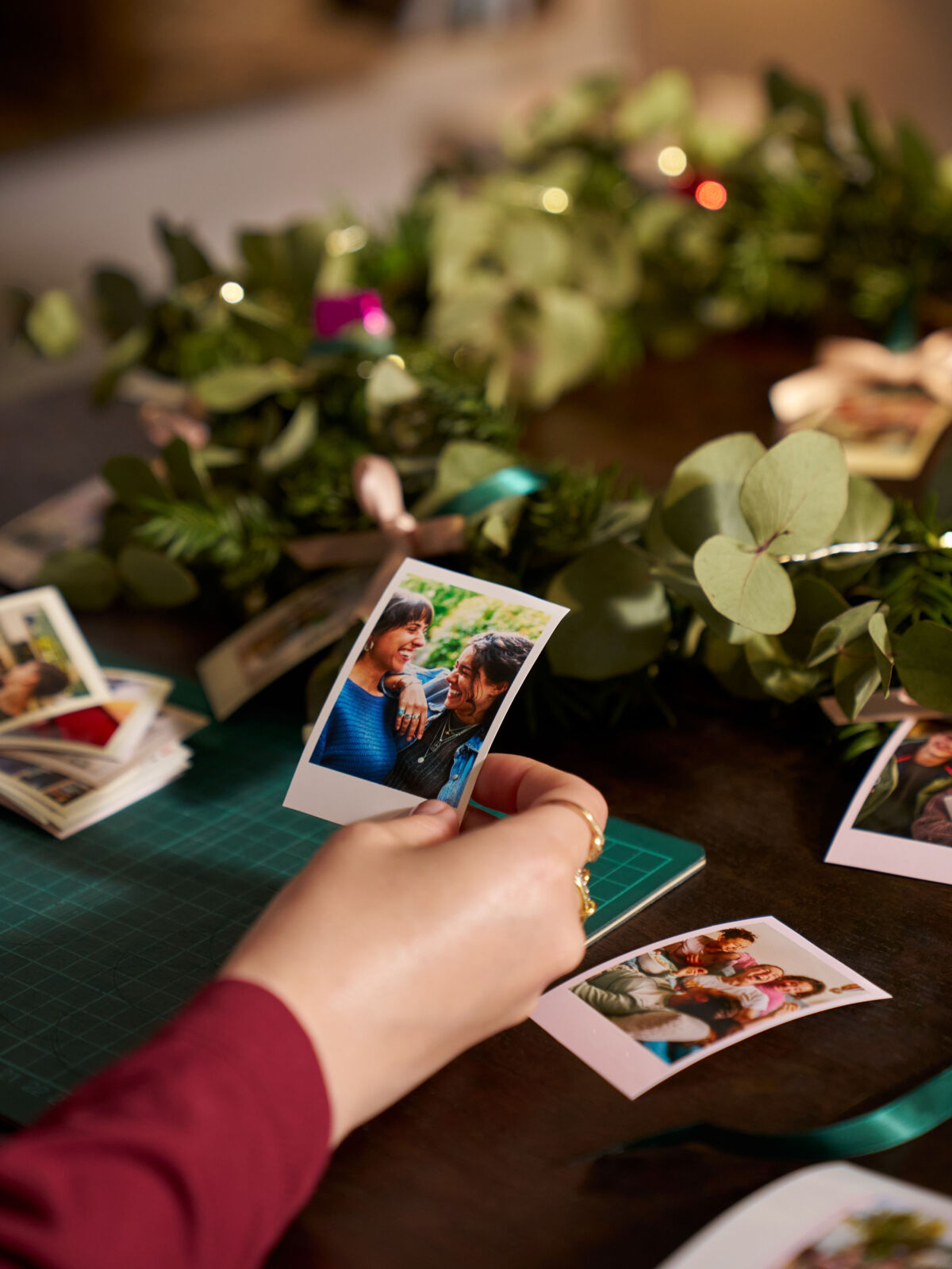 Auf einem Tisch liegt ein weihnachtlicher Kranz sowie ausgedruckte Fotos im Retrostil, die von einer Fau sortiert werden.