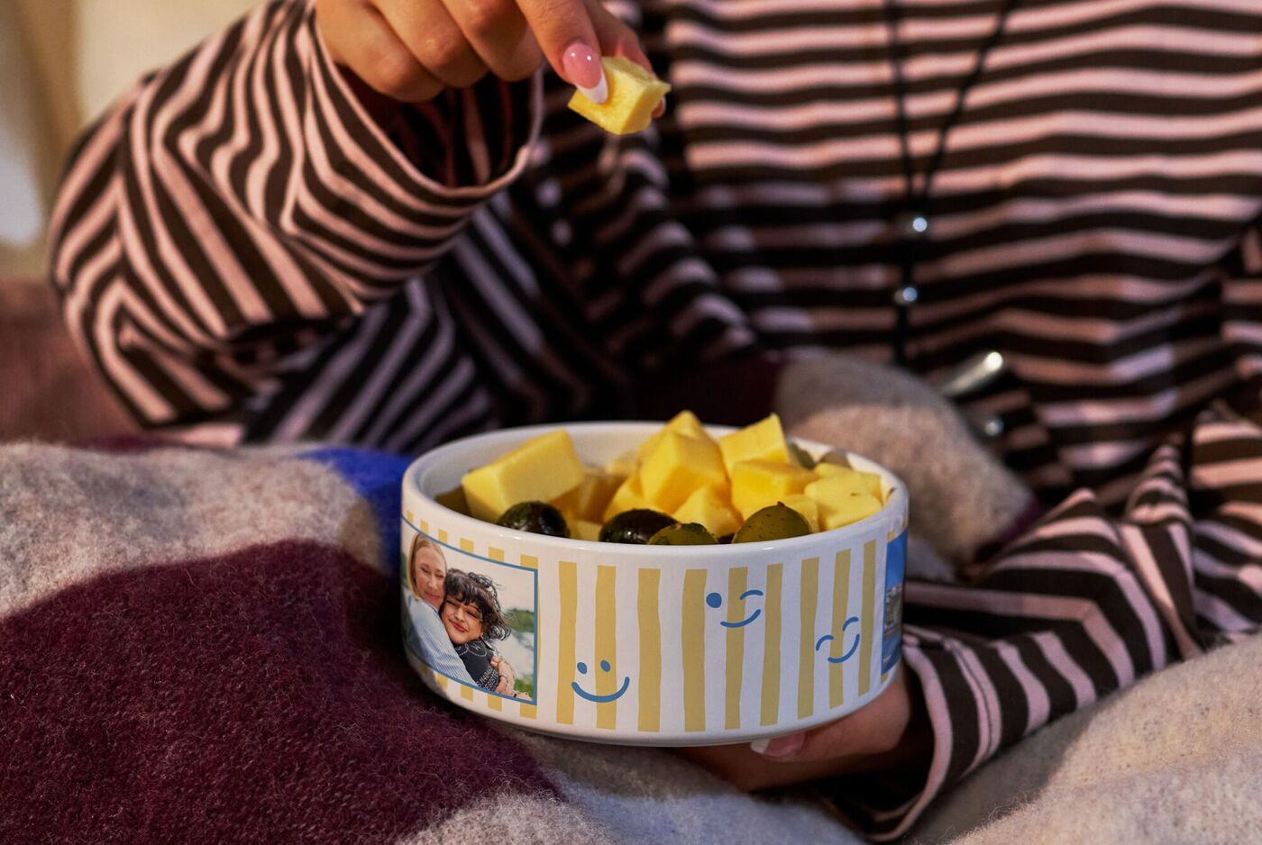 Eine Person mit gestreiftem Pullover genießt Snacks aus einer persönlichen Foto-Snackschale.