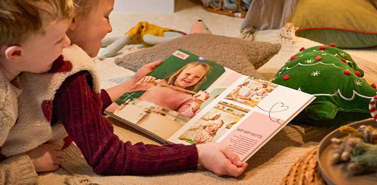 Zwei Kinder betrachten gemeinsam ein CEWE FOTOBUCH mit Familienfotos in weihnachtlicher Umgebung.